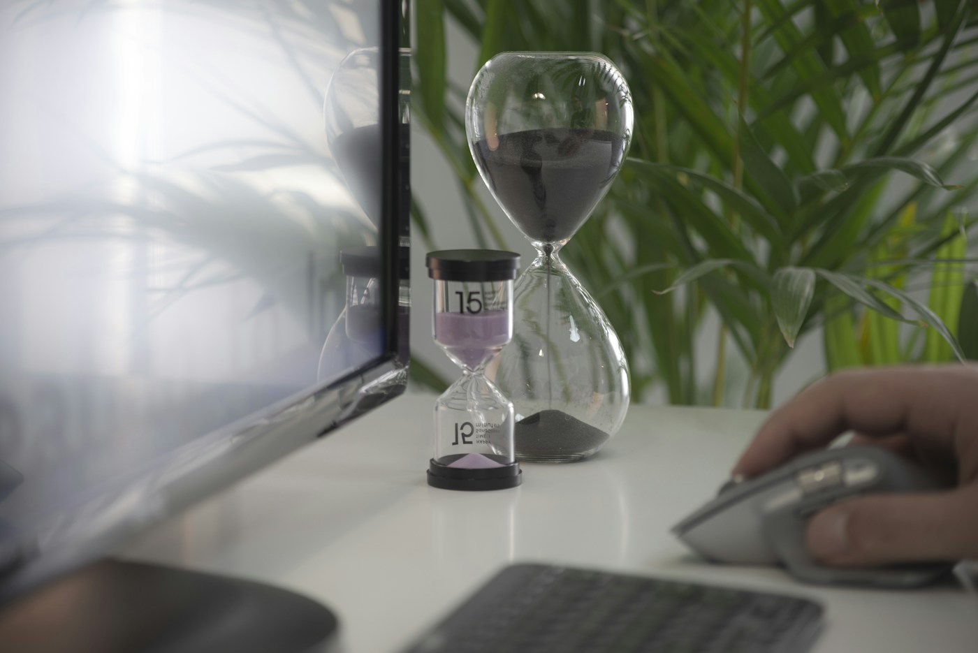 Hourglasses beside a computer, with soft daylight and green foliage