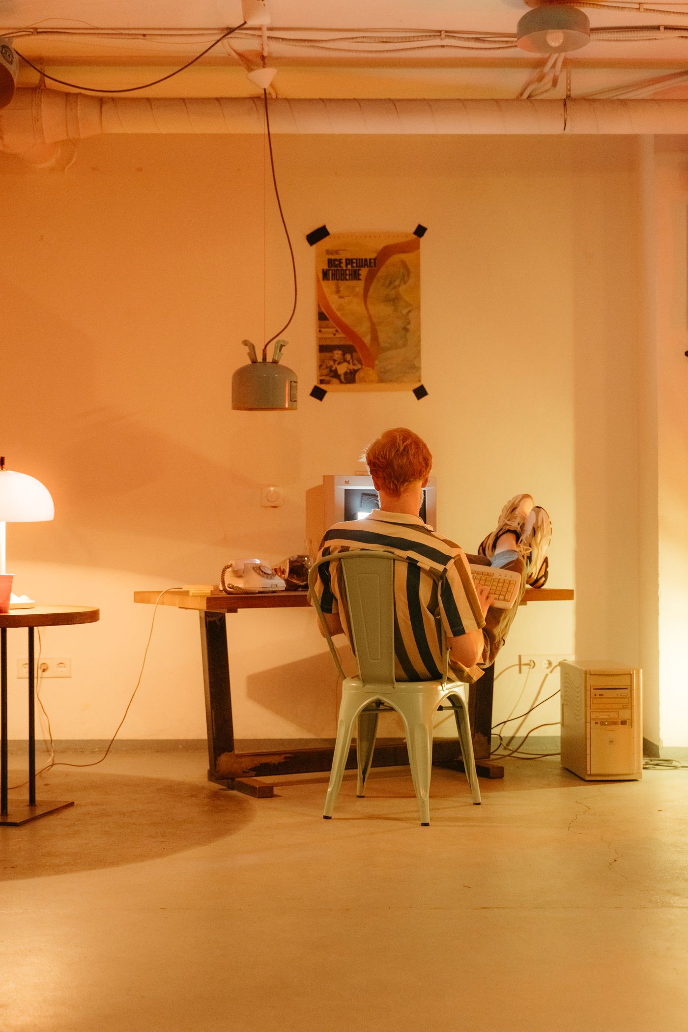 A person relaxing at a vintage desktop computer in a warmly lit room